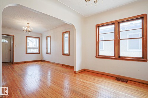Spacious interior featuring wood-finish flooring throughout, an arched doorway, and multiple windows with warm wood trim - 9611 81 Avenue, Edmonton, AB - Indoor Photo Showing Other Room