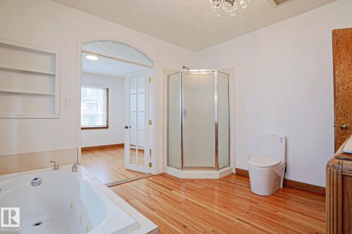 Bathroom featuring wood-finish flooring, a jetted soaking tub, a stand-up shower with frosted glass, and an arched entryway with French doors - 9611 81 Avenue, Edmonton, AB - Indoor
