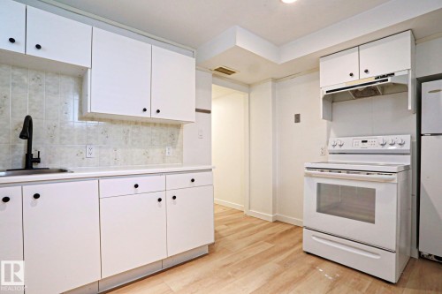 Kitchen featuring white cabinetry, light-toned wood-finish flooring, white countertops, a tile backsplash, and a matte black faucet - 9611 81 Avenue, Edmonton, AB - Indoor Photo Showing Kitchen