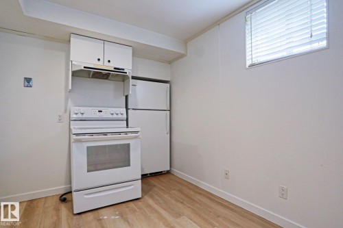 Compact kitchen area featuring a white electric range, coordinating refrigerator, and upper cabinetry - 9611 81 Avenue, Edmonton, AB - Indoor Photo Showing Kitchen