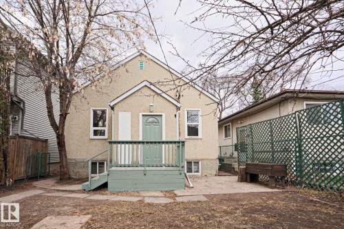 Rear exterior featuring a stucco finish, a covered porch with painted wood railing, an arched entry door, and multiple windows - 9611 81 Avenue, Edmonton, AB - Outdoor With Deck Patio Veranda