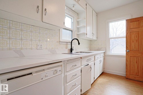 Kitchen featuring white cabinetry, light-toned countertops, a matte black faucet, and patterned tile backsplash - 9611 81 Avenue, Edmonton, AB - Indoor Photo Showing Kitchen