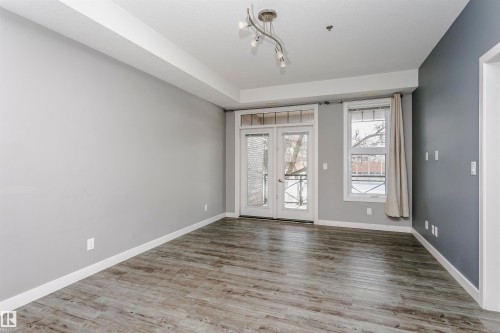 Living area featuring wood-look flooring, light grey walls, and a contrasting dark grey accent wall - 211 10808 71 Avenue, Edmonton, AB - Indoor Photo Showing Other Room