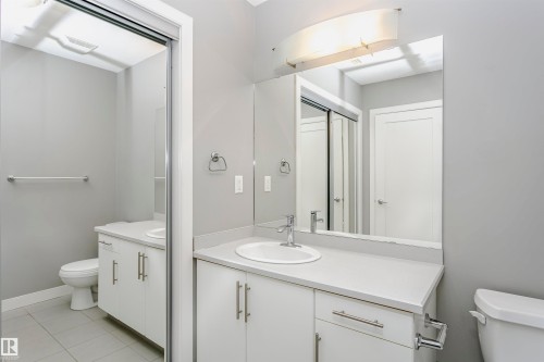 Bathroom featuring a vanity with a white countertop and a white sink, a mirror, and a toilet - 211 10808 71 Avenue, Edmonton, AB - Indoor Photo Showing Bathroom