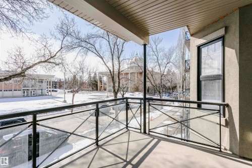 The property features a balcony with a black metal and glass railing, offering views of surrounding trees and a distinct domed building - 211 10808 71 Avenue, Edmonton, AB - Outdoor