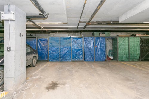 The property features a dedicated parking space in a concrete garage with overhead pipes and lighting - 211 10808 71 Avenue, Edmonton, AB - Indoor Photo Showing Garage
