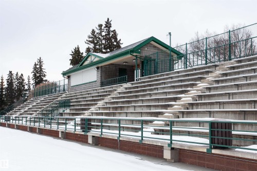 The property offers stadium seating with green railings, a brick building with a dark green roof, and a surrounding fence - 211 10808 71 Avenue, Edmonton, AB - Outdoor