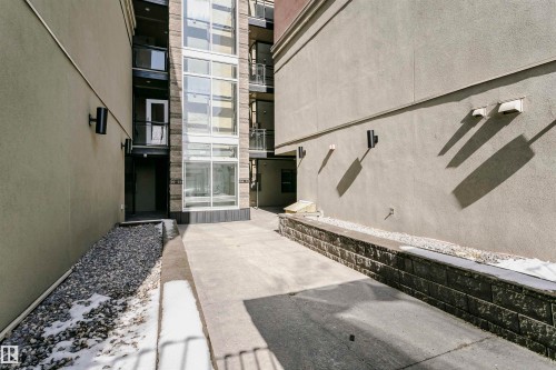 The property features an outdoor concrete walkway, an exterior wall with wall-mounted lighting fixtures, and a retaining wall constructed from stacked stone blocks - 211 10808 71 Avenue, Edmonton, AB -  Photo Showing Other Room
