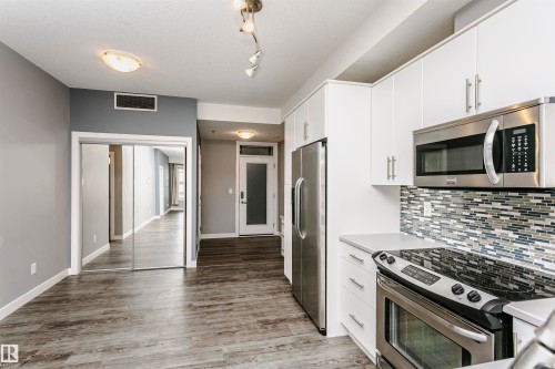 The kitchen features stainless steel appliances, white cabinetry, a light-colored countertop, and a tiled backsplash - 211 10808 71 Avenue, Edmonton, AB - Indoor Photo Showing Kitchen With Stainless Steel Kitchen With Upgraded Kitchen