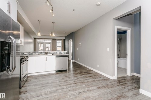 Open concept living area featuring wood-look flooring, a kitchen with stainless steel appliances, white cabinetry, and pendant lighting - 211 10808 71 Avenue, Edmonton, AB - Indoor Photo Showing Kitchen With Double Sink
