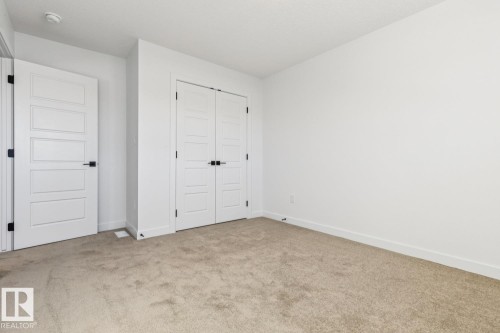 Interior room featuring neutral wall paint, light-toned carpet flooring, white trim, and two white paneled doors with black hardware - 39 Caledon Crescent, Spruce Grove, AB - Indoor Photo Showing Other Room