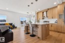 Open-concept kitchen and living area featuring wood-finish flooring, light wood cabinetry, a center island with seating, pendant lighting, and a stainless steel range hood - 39 Caledon Crescent, Spruce Grove, AB  - Indoor Photo Showing Kitchen With Upgraded Kitchen 