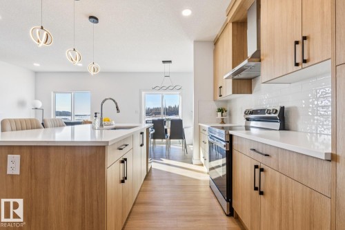 Modern kitchen featuring wood-finish cabinetry, stainless steel appliances, white subway tile backsplash, and an island with an undermount sink and contemporary pendant lighting - 39 Caledon Crescent, Spruce Grove, AB - Indoor Photo Showing Kitchen With Upgraded Kitchen