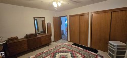 Bedroom featuring two sets of sliding closet doors with wood-finish panels, neutral carpeting, and a ceiling fan with integrated lighting - 