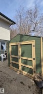 Green storage shed featuring a pitched roof, double doors with light-toned trim, and metal hardware - 