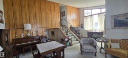 Split-level interior featuring extensive wood paneling, a grand staircase with ornate metal railings, and a large front window with transom detail - 