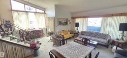 Spacious living area featuring high ceilings, large windows with vertical blinds, and a built-in staircase with decorative wrought iron railing - 