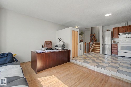 Open-concept living space featuring wood-finish flooring, a raised kitchen area with checkered tile, wood cabinetry, and stainless steel appliances - 4106 38 Street, Edmonton, AB - Indoor
