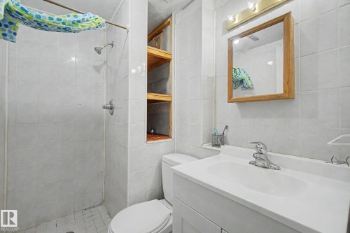 Bathroom featuring a shower stall with tile surround, built-in shelving, a single vanity with an integrated sink, and a framed mirror with overhead lighting - 4106 38 Street, Edmonton, AB - Indoor Photo Showing Bathroom