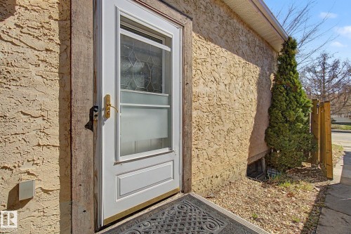 White storm door with decorative glass inserts, textured stucco exterior, and a gravel-covered ground - 4106 38 Street, Edmonton, AB - Outdoor