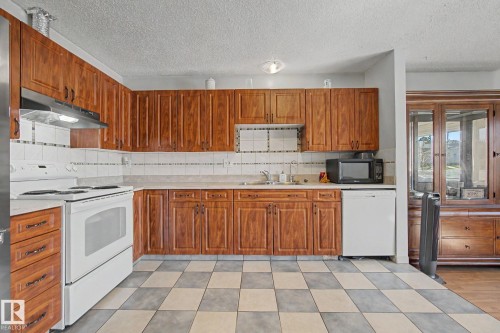 Kitchen featuring ample wood cabinetry, a white tile backsplash, and a checkerboard floor pattern - 4106 38 Street, Edmonton, AB - Indoor Photo Showing Kitchen With Double Sink