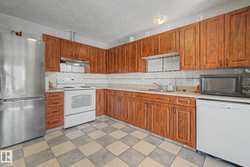 Kitchen featuring wood-finish cabinetry, a checkerboard tile floor, and a white tile backsplash - 4106 38 Street, Edmonton, AB - Indoor Photo Showing Kitchen With Double Sink