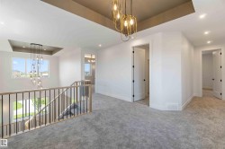 Spacious landing featuring plush grey carpeting, contemporary chandelier lighting, and a modern stair railing with wood-finish top rail and black balusters - 