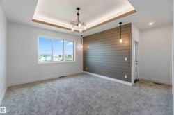 Spacious room featuring a tray ceiling with integrated lighting, a contemporary chandelier, and a shiplap accent wall - 