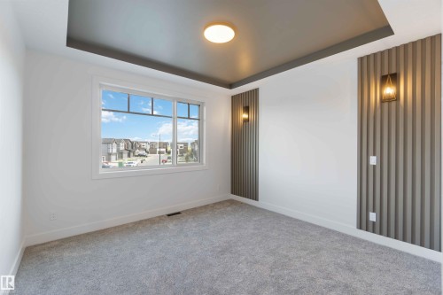 Spacious room featuring a white window frame, contemporary ceiling design, modern flush-mount light fixture, and two decorative wall sconces illuminating fluted wall panels - 74 Eldridge Point(E), St. Albert, AB - Indoor Photo Showing Other Room