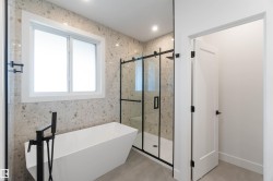 Modern bathroom featuring a freestanding soaking tub with a matte black floor-mounted faucet, a spacious walk-in shower with a glass enclosure, large format speckled wall tiles, and light-toned flooring - 
