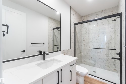 Modern bathroom featuring a glass-enclosed shower with speckled wall tile, a white vanity with quartz countertop, an undermount sink, and black fixtures - 74 Eldridge Point(E), St. Albert, AB - Indoor Photo Showing Bathroom