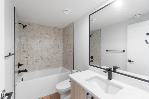 Contemporary bathroom featuring a tub/shower combination with speckled tile surround, a single vanity with a white countertop and integrated sink, and matte black hardware - 74 Eldridge Point(E), St. Albert, AB - Indoor Photo Showing Bathroom