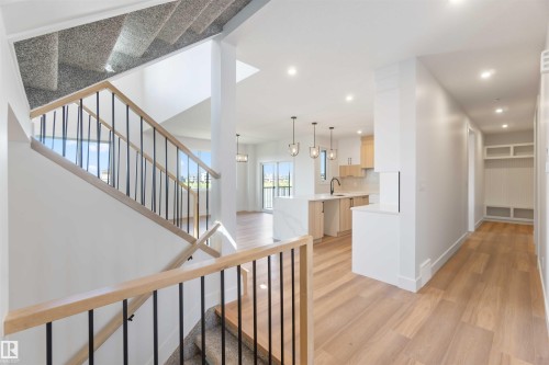 Open-concept interior featuring wood-finish flooring, a modern staircase with wood handrails and black balusters, recessed lighting, a contemporary kitchen with light-toned cabinetry and pendant lights, and a built-in storage bench - 74 Eldridge Point(E), St. Albert, AB - Indoor Photo Showing Other Room