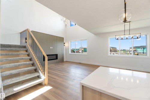 Spacious interior featuring a carpeted staircase with wood and metal railing, a built-in electric fireplace, wood-finish flooring, high vaulted ceilings, and a quartz countertop island - 74 Eldridge Point(E), St. Albert, AB - Indoor Photo Showing Other Room