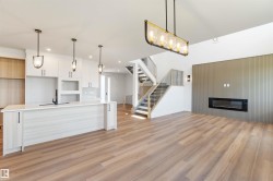 Open-concept living area featuring wood-finish flooring, a contemporary linear fireplace set against a textured accent wall, and a modern kitchen island with pendant lighting - 