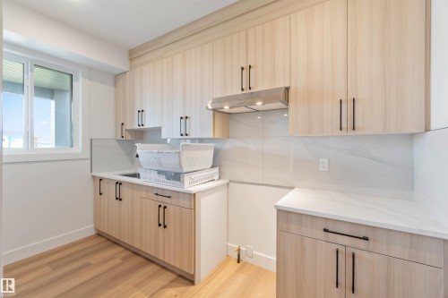 Utility room featuring wood-finish cabinetry with black hardware, white countertops, and a white tile backsplash - 74 Eldridge Point(E), St. Albert, AB - Indoor Photo Showing Kitchen