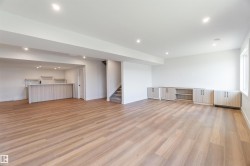 Spacious open-concept lower level featuring wood-finish flooring, recessed lighting, and a built-in wet bar with upper shelving - 