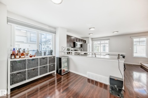 Open-concept living space with dark wood-finish flooring, recessed ceiling lighting, and a kitchen featuring dark cabinetry, stainless steel appliances, and a light-toned countertop - 45 4850 Terwillegar Common, Edmonton, AB - Indoor Photo Showing Other Room