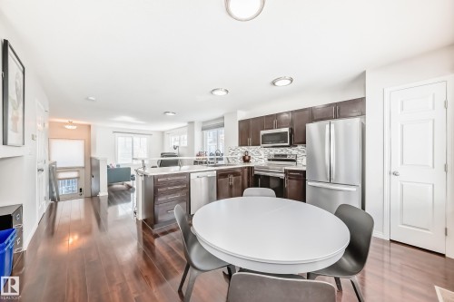 Kitchen and dining area featuring rich wood-finish flooring, dark wood cabinetry, stainless steel appliances, and a tiled backsplash - 45 4850 Terwillegar Common, Edmonton, AB - Indoor