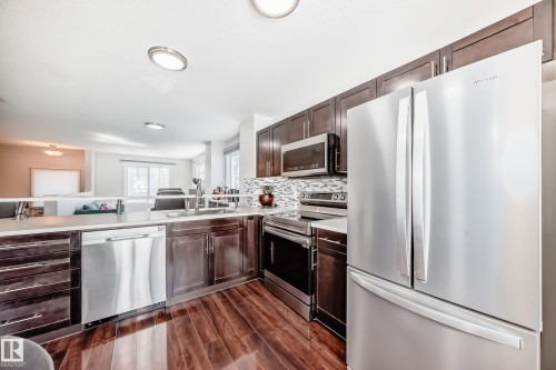 Kitchen featuring stainless steel appliances, dark wood cabinetry, and wood-finish flooring - 45 4850 Terwillegar Common, Edmonton, AB - Indoor Photo Showing Kitchen With Double Sink With Upgraded Kitchen