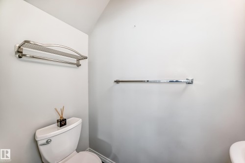 White toilet with a chrome flush lever, a wall-mounted chrome towel bar, and a brushed nickel towel shelf - 45 4850 Terwillegar Common, Edmonton, AB - Indoor Photo Showing Bathroom