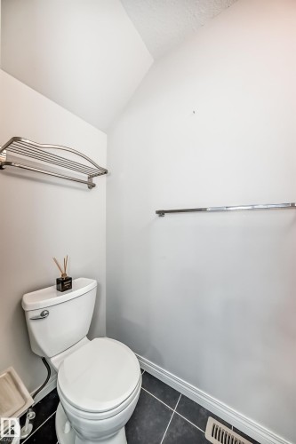 Compact bathroom featuring a white toilet, black tile flooring with white grout, and a white baseboard trim - 45 4850 Terwillegar Common, Edmonton, AB - Indoor Photo Showing Bathroom