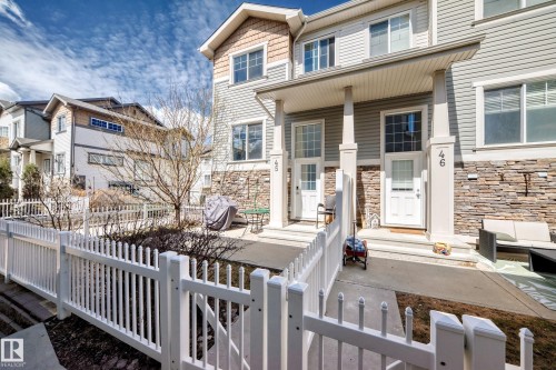 Modern townhome exterior featuring light gray siding, stone veneer accents, and a white picket fence - 45 4850 Terwillegar Common, Edmonton, AB - Outdoor With Deck Patio Veranda