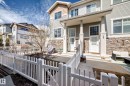 Modern townhome exterior featuring light gray siding, stone veneer accents, and a white picket fence - 45 4850 Terwillegar Common, Edmonton, AB  - Outdoor With Deck Patio Veranda 