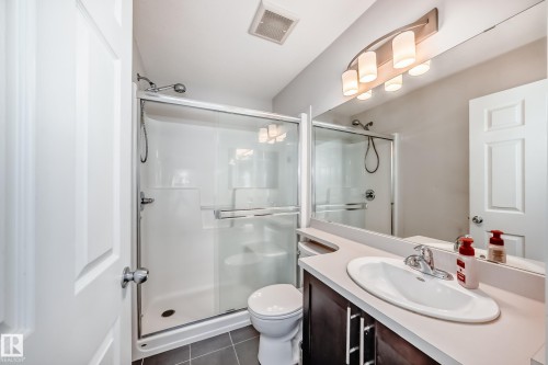 Contemporary bathroom featuring a glass-enclosed shower, dark wood-finish vanity with a light countertop, integrated sink, and an expansive mirror with a multi-bulb light fixture - 45 4850 Terwillegar Common, Edmonton, AB - Indoor Photo Showing Bathroom