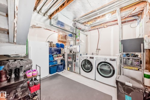 Dedicated utility space featuring a front-loading washer and dryer set, an additional refrigerator, and exposed ceiling joists - 45 4850 Terwillegar Common, Edmonton, AB - Indoor Photo Showing Laundry Room