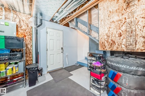 Basement area featuring a painted concrete floor, exposed ceiling joists, a finished stairway with wood railings, and a six-panel door - 45 4850 Terwillegar Common, Edmonton, AB - 
