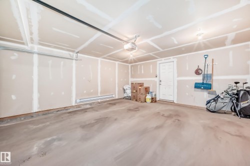 Attached two-car garage featuring exposed drywall, concrete flooring, and a side-entry door - 45 4850 Terwillegar Common, Edmonton, AB - Indoor Photo Showing Garage