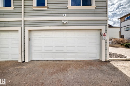 Exterior featuring horizontal siding, white panel garage door, and light fixture - 45 4850 Terwillegar Common, Edmonton, AB - Outdoor With Exterior