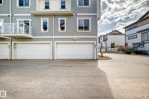 Grey vinyl siding exterior with white trim, featuring three integrated garage doors, a private balcony with white railings, and multiple windows - 45 4850 Terwillegar Common, Edmonton, AB - Outdoor